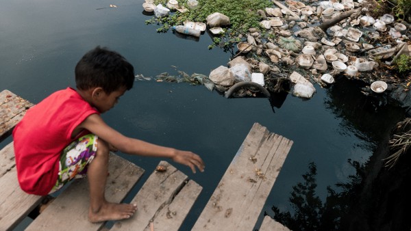 child playing at a garbage-filled lake