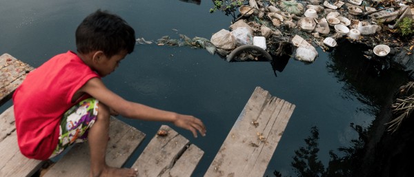 child playing at a garbage-filled lake