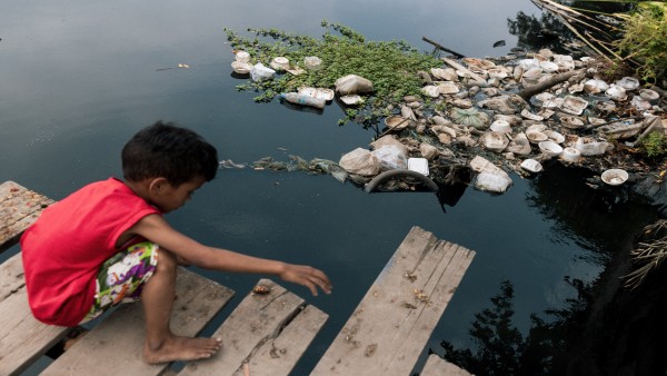 child playing at a garbage-filled lake