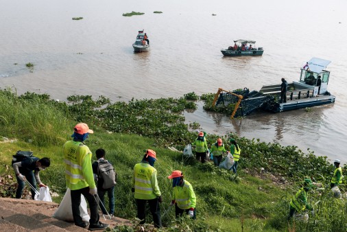 people on land, and a ship on sea collecting gargabe