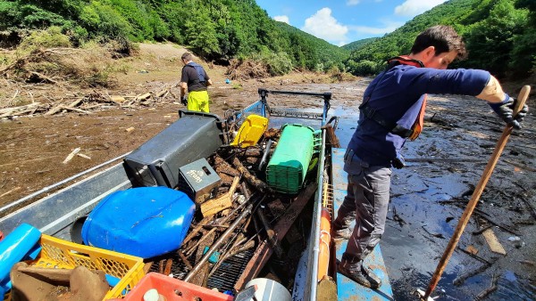 Auf einem Boot fischt ein Mann Müll aus einem Fluss