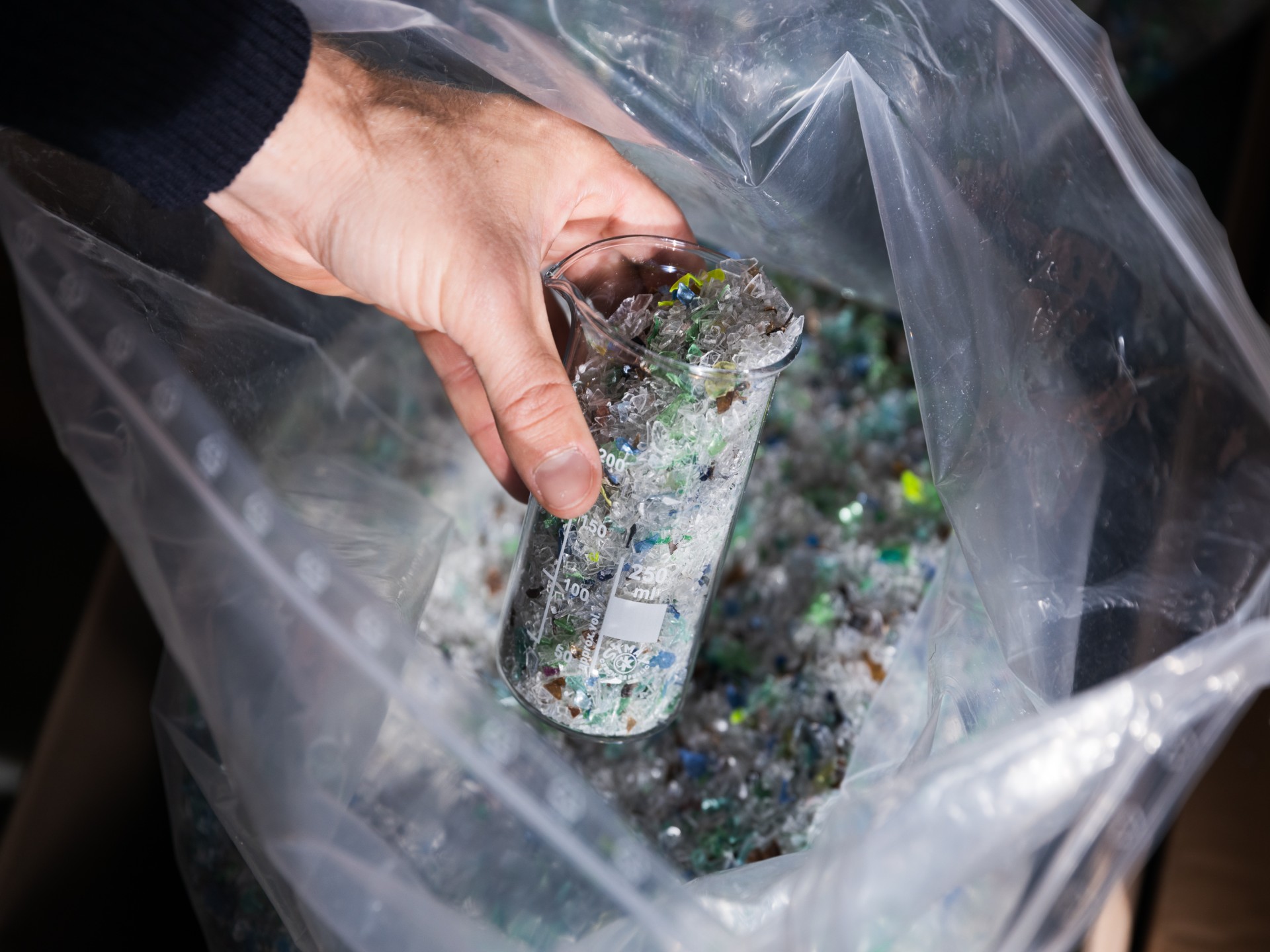 Hand hält einen gläserenen Messbecher gefüllt mit Plastikkleinteilen