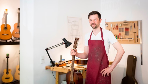 Martin Meckbach hält eine Gitarre am Hals und blickt in die Kamera