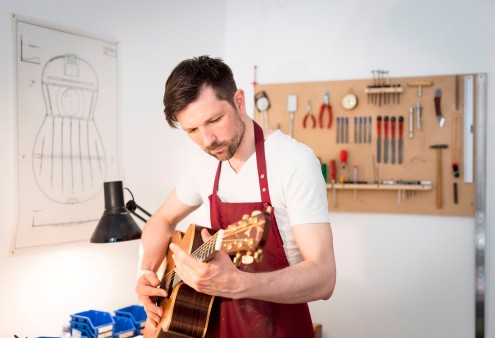 Martin Meckbach steht in seinem Laden und stimmt eine Gitarre