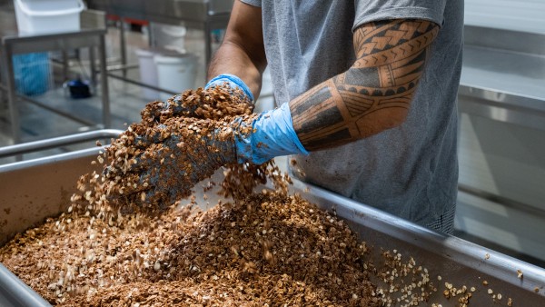 Eine Person mischt mit Gummihandschuhen Müsli in einem großen Behälter