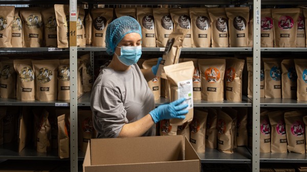 Eine Person mit Hygiene-Schutzkleidung packt Müsli in einen Karton