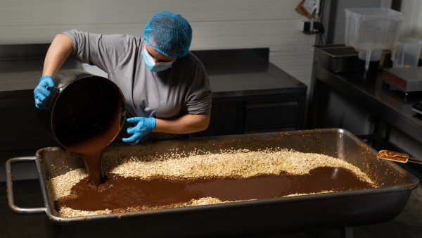 Eine Mitarbeiterin gießt Müsli aus einem Eimer in einen großen Behälter