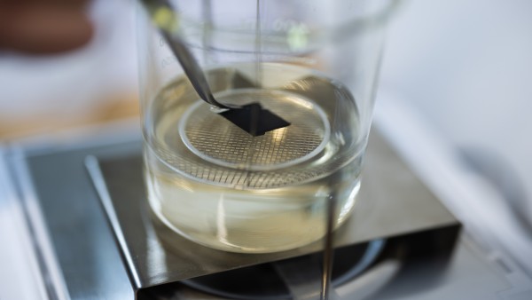 Plastik wird mit einer Pinzette in ein Becherglas gehalten, das auf einer Heizplatte steht. 