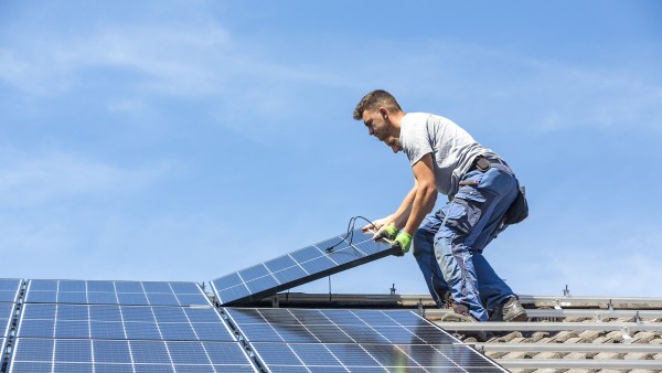 Ein Bauarbeiter auf einem Hausdach beim Verlegen eines Solarpanels