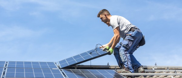 Ein Bauarbeiter auf einem Hausdach beim Verlegen eines Solarpanels