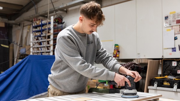Ein Hodapps Werkamitarbeiter schleift ein Holzstück mit einem modernen Gerät glatt. 
