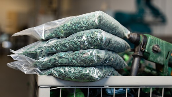 Aussortierte Bohrmaschinen in einer großen Kiste zusammen mit Tüten, die mit grünem Plastikgranulat gefüllt sind.