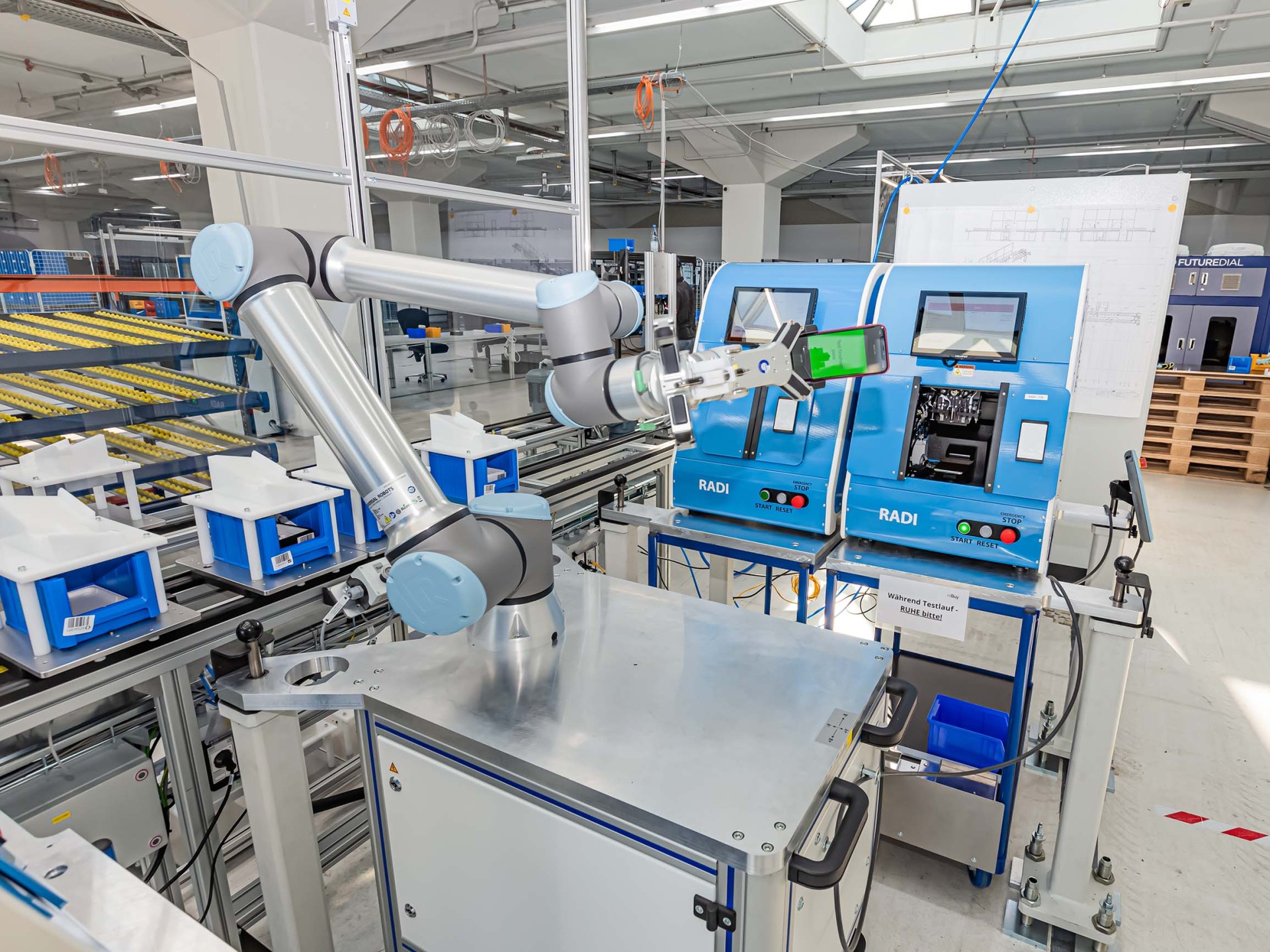 In a production hall, a robotic arm holds a smartphone. 