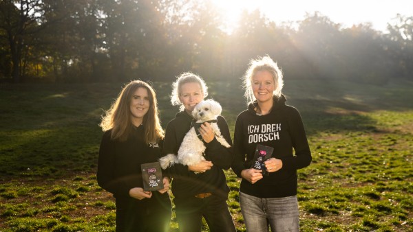 drei junge Frauen stehen auf einer Wiese mit einem Hund
