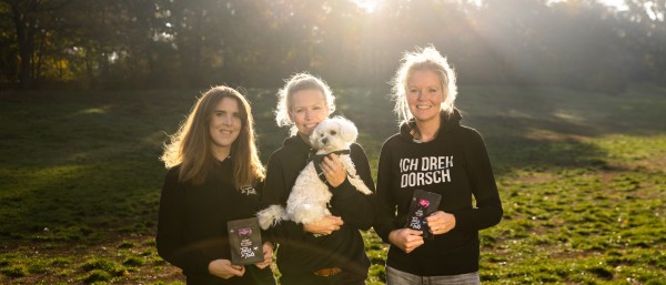 drei junge Frauen stehen auf einer Wiese mit einem Hund