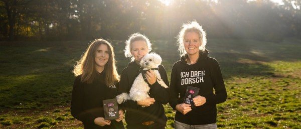 three young women and a dog standing on a meadow 