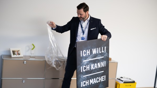 weLOG Gründer Manuel Rupp in seinem Büro in Wetzlar hält ein Bild mit einem Motivationsspruch in der Hand