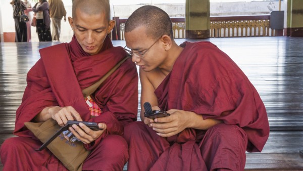 Two Buddhist monks sit on the steps to the Shwedagon Pagoda with a smartphone in their hands
