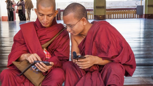 Two Buddhist monks sit on the steps to the Shwedagon Pagoda with a smartphone in their hands