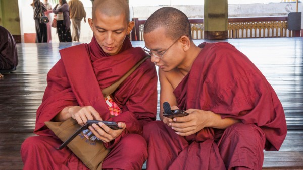 Two Buddhist monks sit on the steps to the Shwedagon Pagoda with a smartphone in their hands