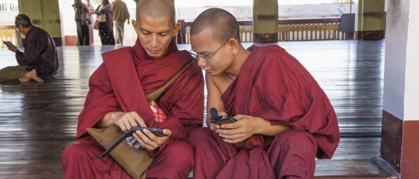 Zwei buddhistische Mönche in Myanmar sitzen auf den Stufen zur Pagode Shwedagon und schauen auf ihre Smartphones