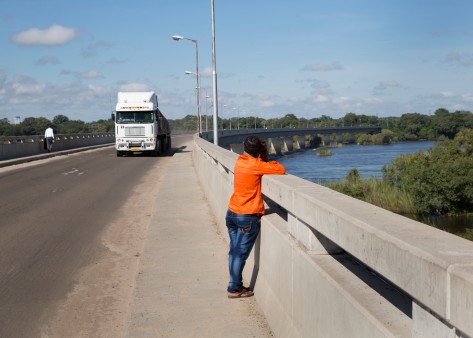 A man stands on the bridge, looking down into the water