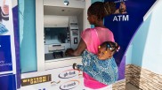 Frau mit Kind bezahlt in Ghana an einem Bankautomaten