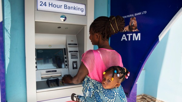 Frau mit Kind bezahlt in Ghana an einem Bankautomaten