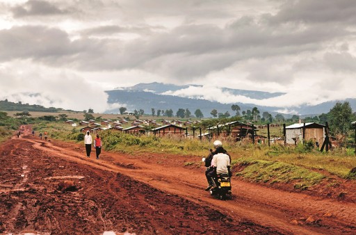 Eine ländliche Straße in dünn besiedelter Region, auf der ein Mofa und zwei Fußgänger zu sehen sind