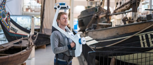 Mann mit mobilem Vermessungsgerät in Lagerhalle mit Booten