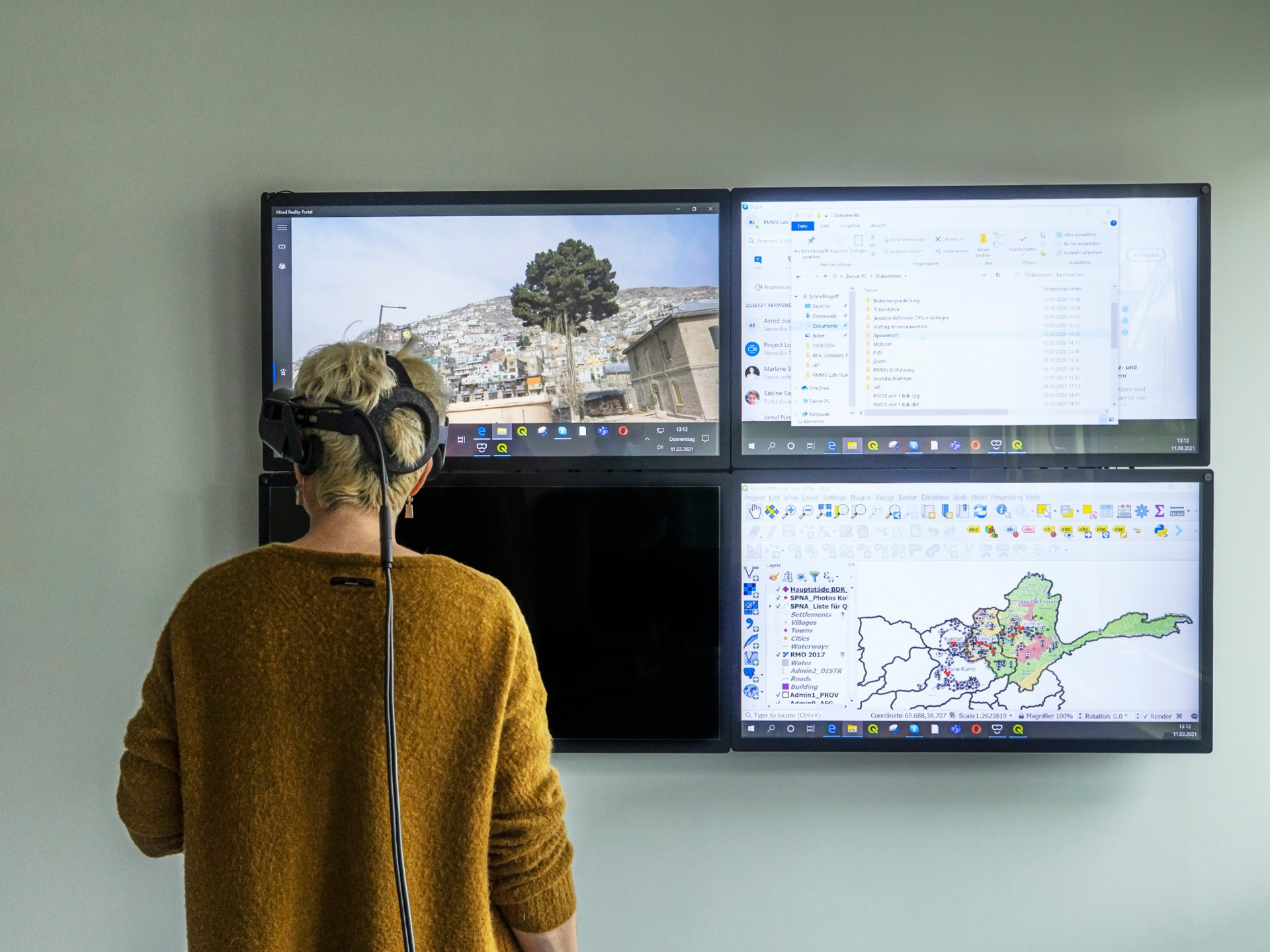 A woman looks at four suspended screens with maps and houses