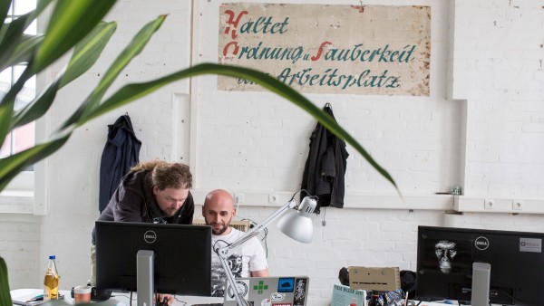 Zwei Rhebo-Mitarbeiter vor Sinnspruch an der Wand im Büro