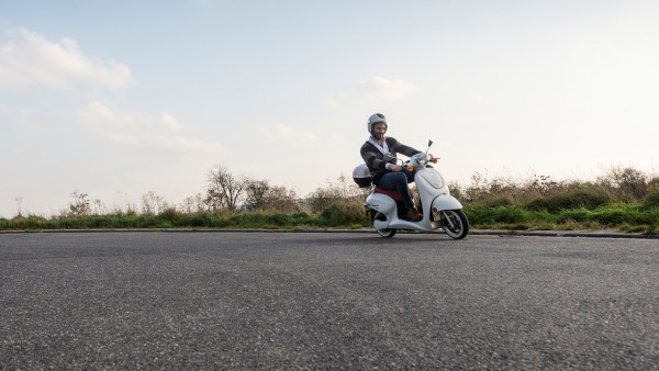 Auf einer asphaltierten Straße fährt ein Mann auf einem Roller