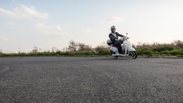 Auf einer asphaltierten Straße fährt ein Mann auf einem Roller