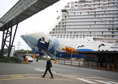 Ein Mitarbeiter geht durch den Hafen, hinter ihm thront das neue Kreuzfahrtschiff