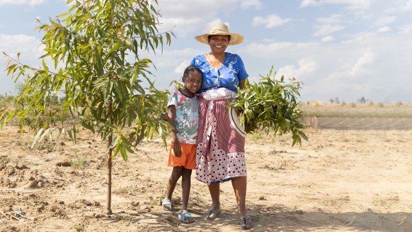 Wiederaufforstungsprojekt in Madagaskar. Eine Frau steht mit ihrem Kind neben einer der neu gepflanzten Bäume.