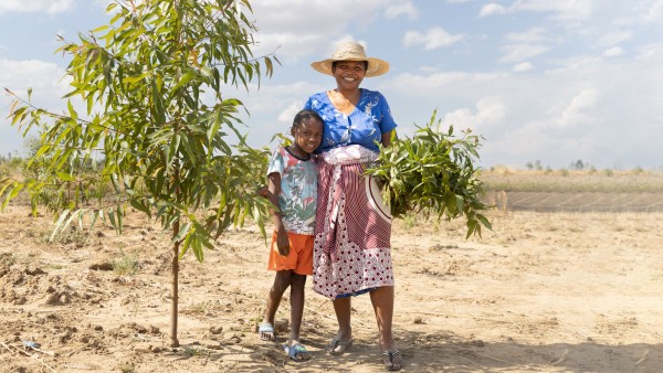 Wiederaufforstungsprojekt in Madagaskar. Eine Frau steht mit ihrem Kind neben einer der neu gepflanzten Bäume.