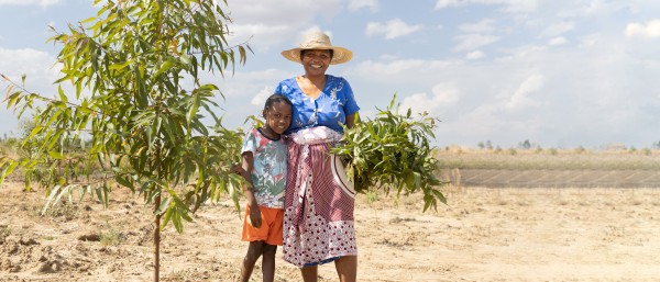 Wiederaufforstungsprojekt in Madagaskar. Eine Frau steht mit ihrem Kind neben einer der neu gepflanzten Bäume.